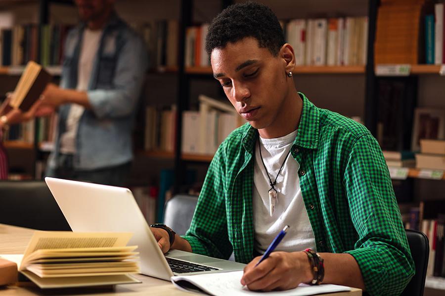 Image of a student in front of a laptop and writing on a notepad